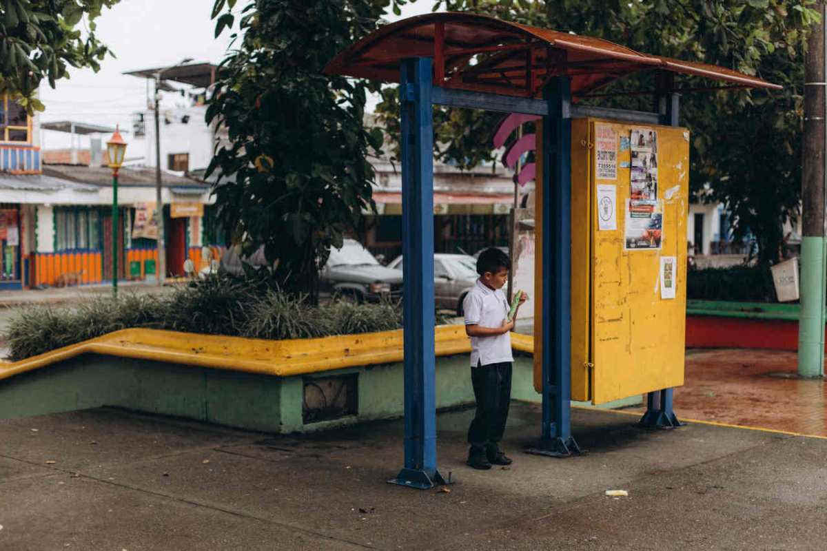 A child stands at a colorful outdoor waiting shed, immersed in thought.